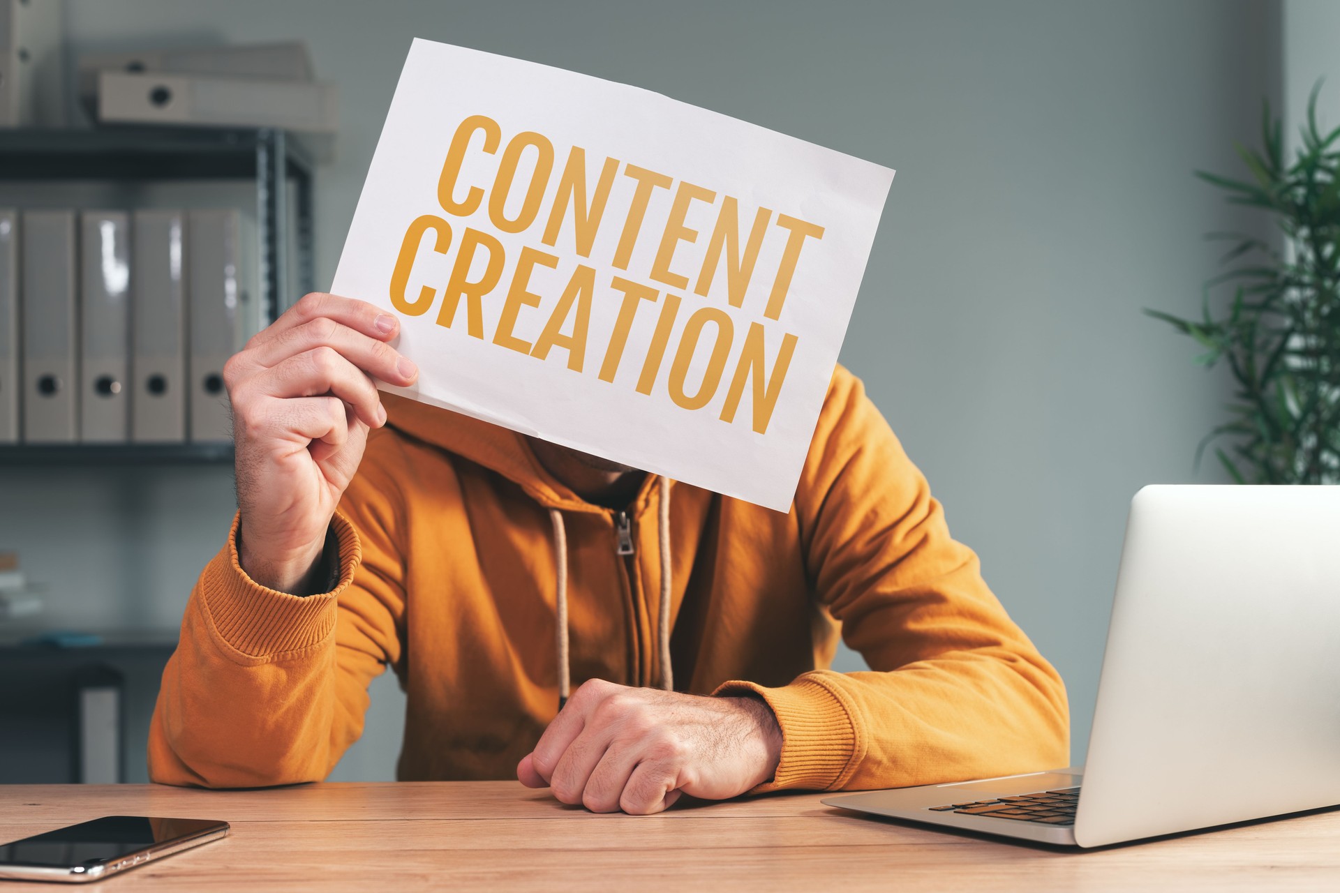 Content creation, man holding paper in front of his face in home office interior