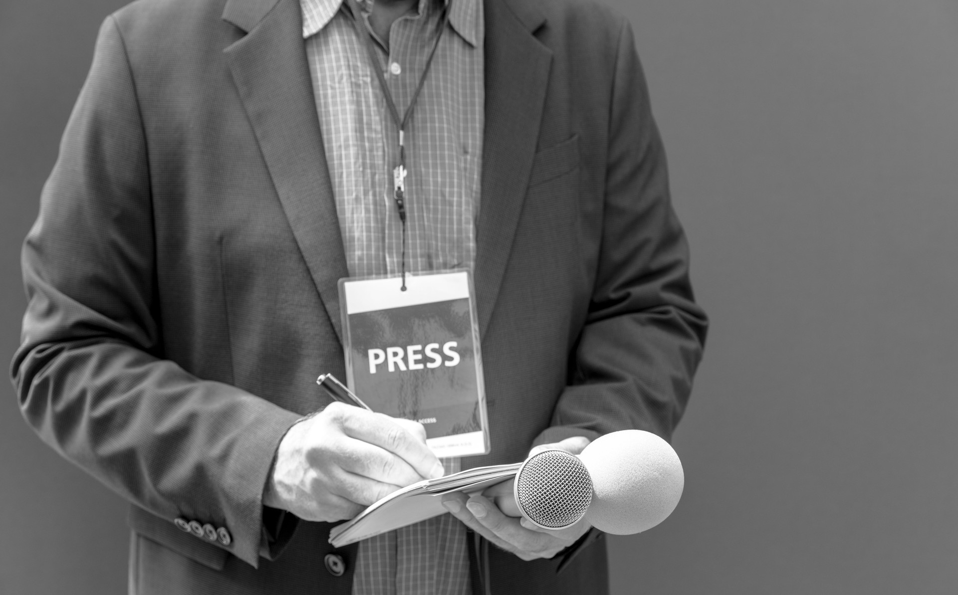 Correspondent or reporter with press pass at media event, holding microphone, writing notes. Journalism concept with copy space.